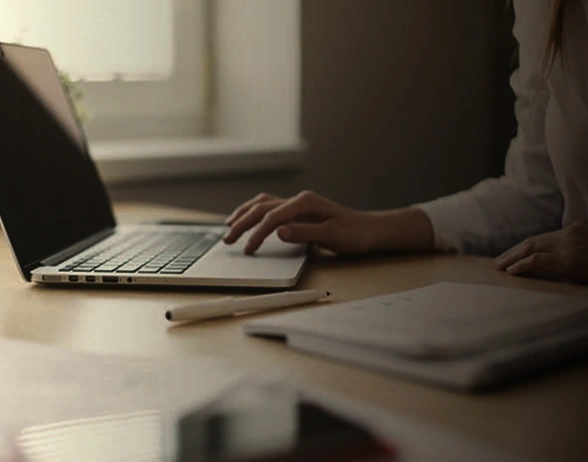 Person working on laptop at desk with notebook and stylus