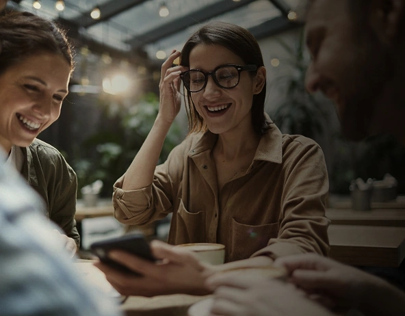 Friends smiling and looking at smartphone together in café