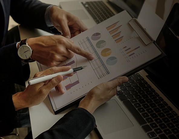 Colleagues analyzing charts and data on clipboard next to laptop