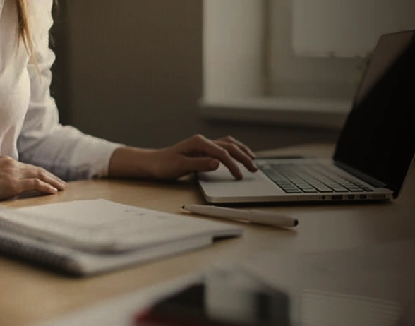 Person working on laptop at desk with notebook and stylus