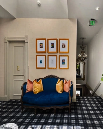 Vintage blue sofa with colorful pillows in a hotel lobby with framed artwork and patterned carpet
