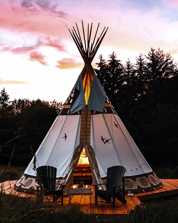 Glamping teepee tent at sunset with outdoor seating and warm interior lighting