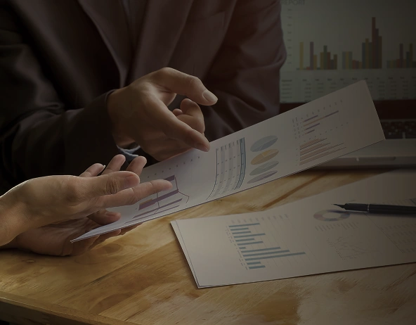 Two people discussing charts and reports at desk with printed analytics