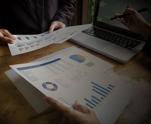 Team reviewing charts and financial reports on table with laptop