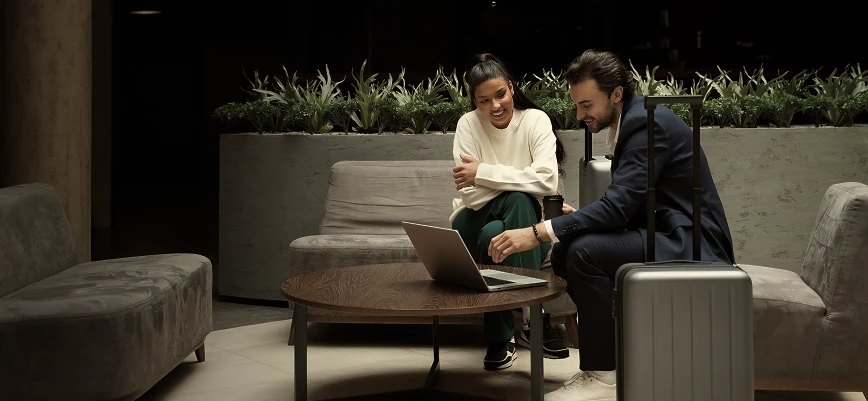 Travelers with suitcase working on laptop in hotel lounge