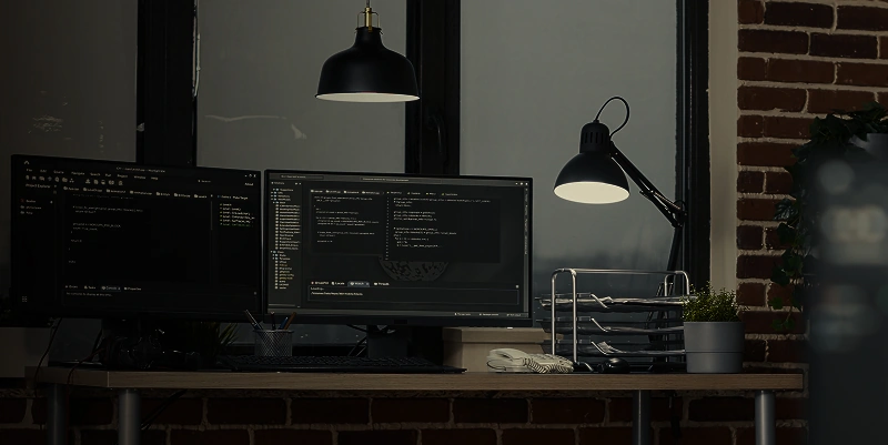 Modern workspace with dual monitors displaying code in a dimly lit office