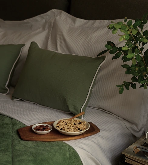 Hotel bed with green pillows and breakfast tray with snacks