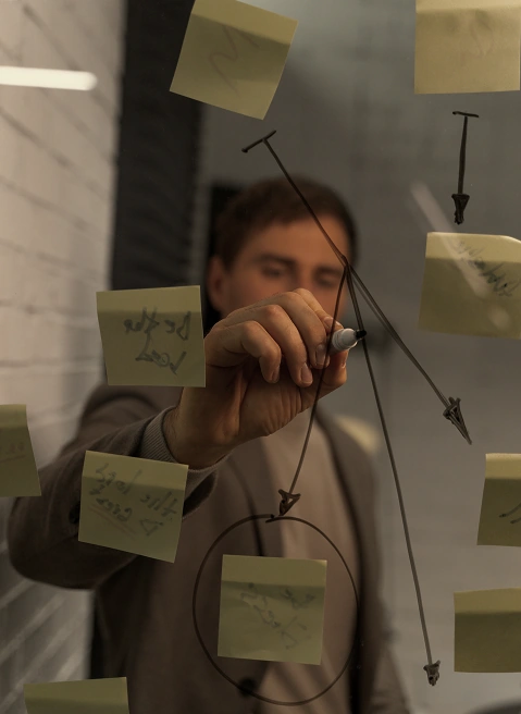 Person drawing strategy diagram on glass board with sticky notes